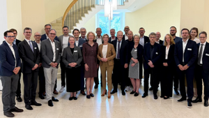Gruppenbild. Eine Gruppe an Menschen stehen vor einer runden Treppe