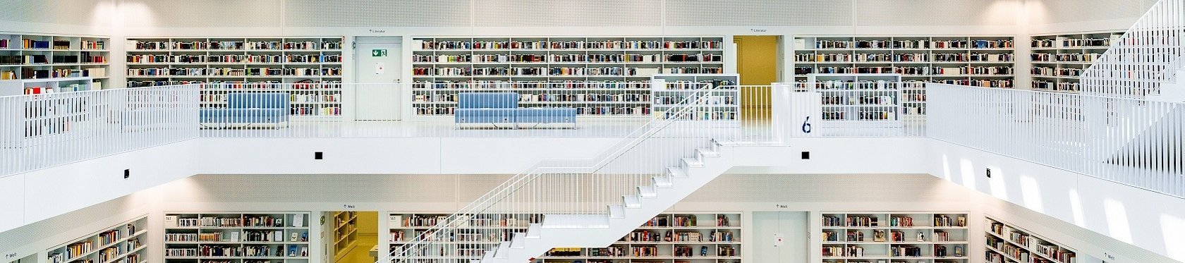 in Bild des Innenraums der Stuttgarter Stadtbibliothek. Helle Weiße treppen in einem gebäude mit einem Mittleren hohlen kern an welchen die Stockwerke in Balkonen grenzen 