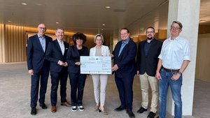 Auf dem Foto halten sieben Personen gemeinsam einen Scheck in der Hand