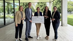 Gruppe von Menschen, eine Frau hält einen symbolischen Scheck hoch