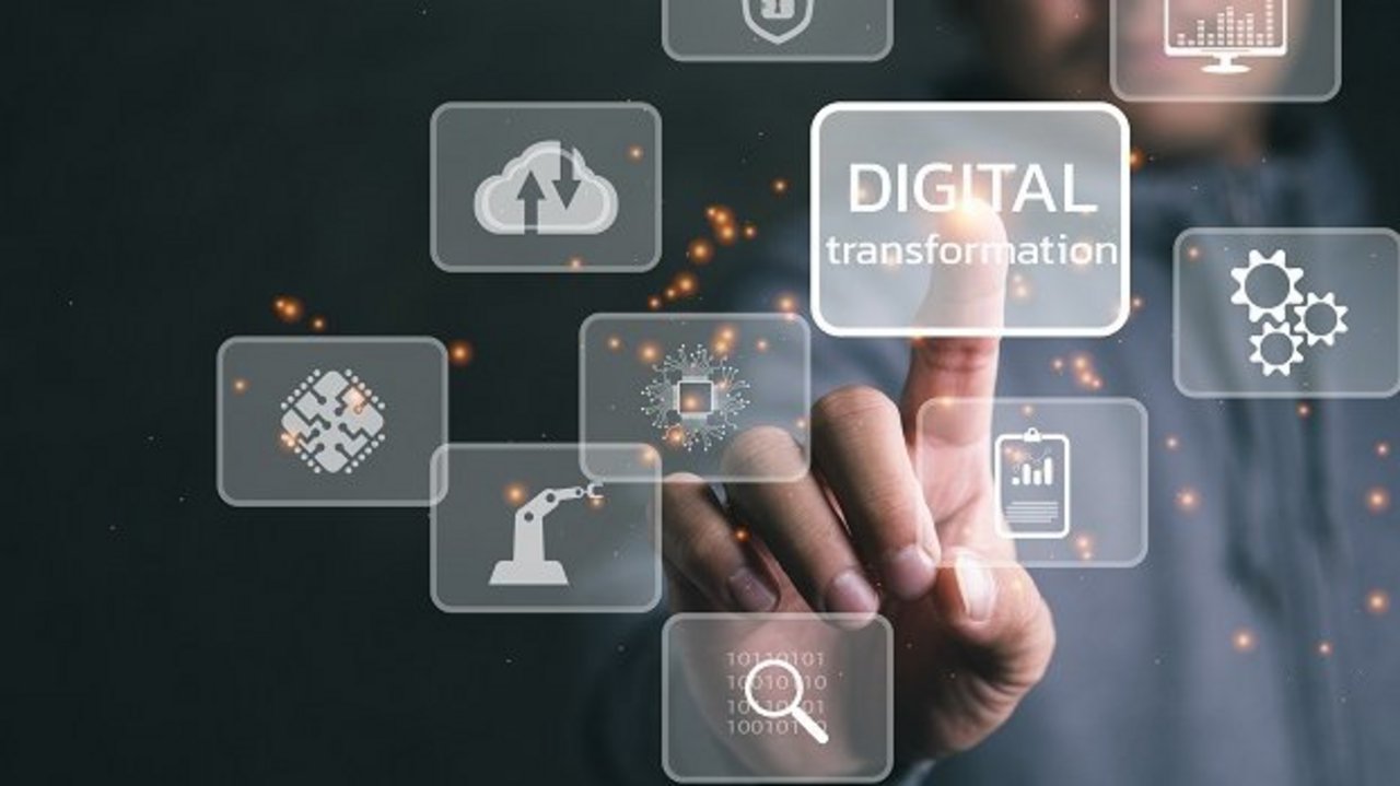 Eine Person berührt mit dem Finger ein transparentes Icon mit der Aufschrift „Digital transformation“. Um das Hauptsymbol herum schweben weitere digitale Symbole, darunter Zahnräder, Cloud, Roboterarm und Mikrochip.