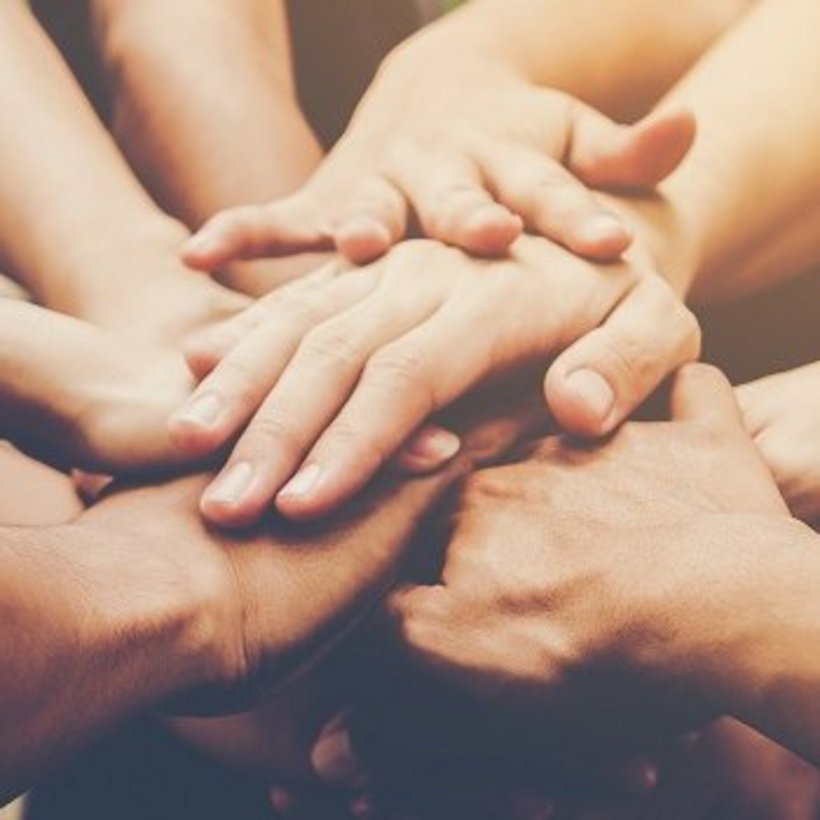 Mehrere Hände von unterschiedlichen Personen liegen übereinander in der Mitte, als Symbol für Zusammenhalt, Teamgeist und Kooperation.