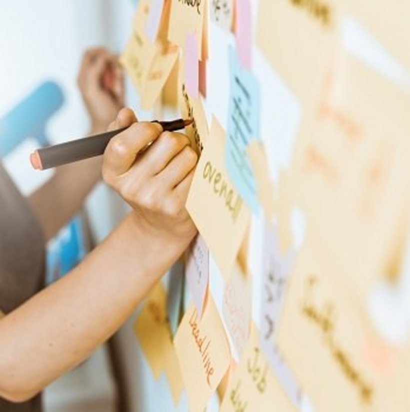 Eine Wand mit Post-Its und eine Frau die darauf schreibt