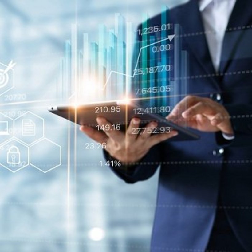 Geschäftsperson im Anzug hält ein Tablet, auf dem leuchtende Balkendiagramme und Finanzdaten eingeblendet sind. Links im Bild schweben Symbole für digitale Anwendungen wie Einkauf, Cloud, Sicherheit und Kommunikation.