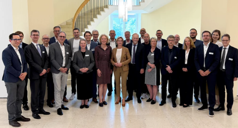 Gruppenbild. Eine Gruppe an Menschen stehen vor einer runden Treppe